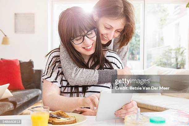 woman embraces girlfriend looking a digital tablet - leaninlgbt stock pictures, royalty-free photos & images