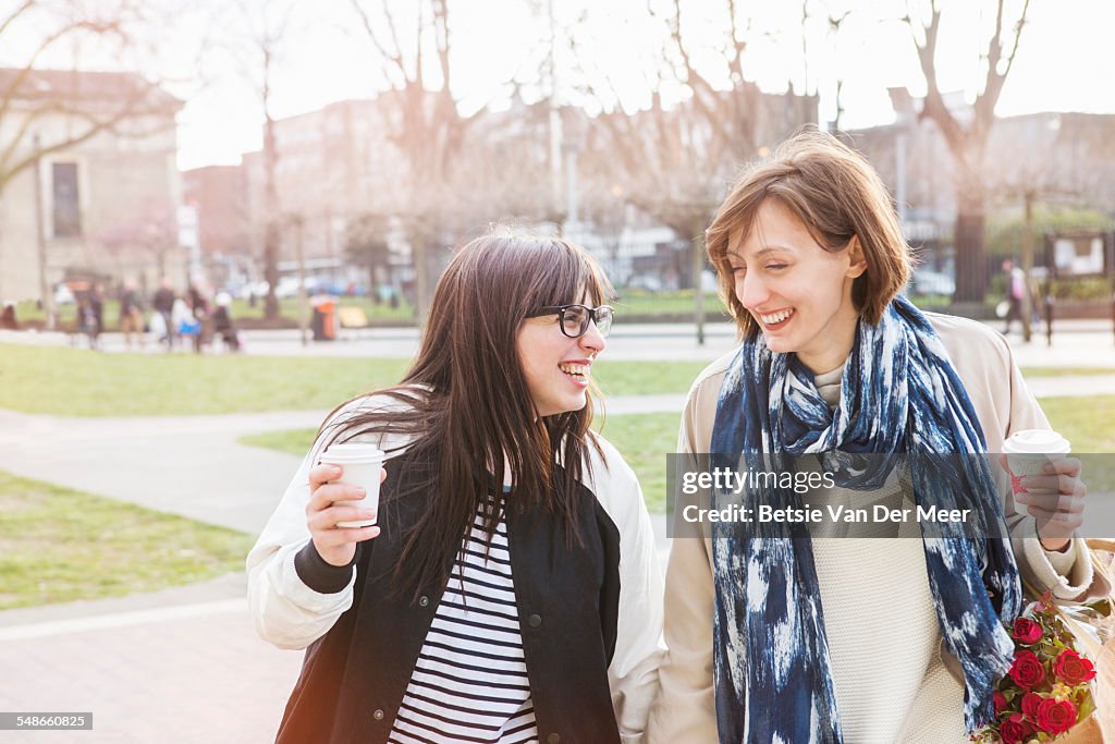 Lesbian couple laughing walking in urban square.