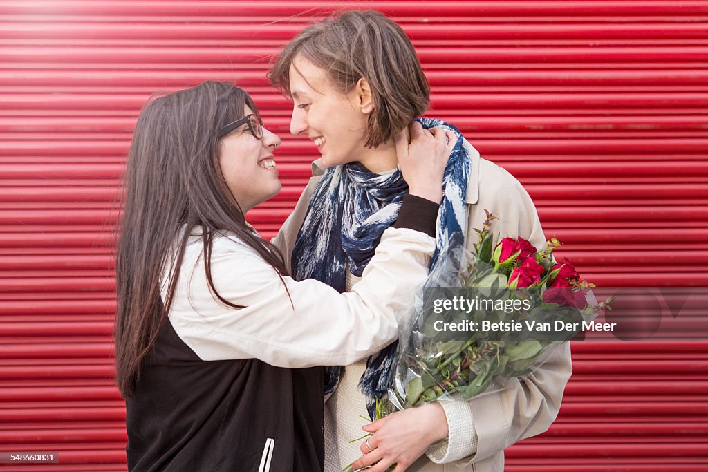 Lesbian couple embracing in front of red shutters.