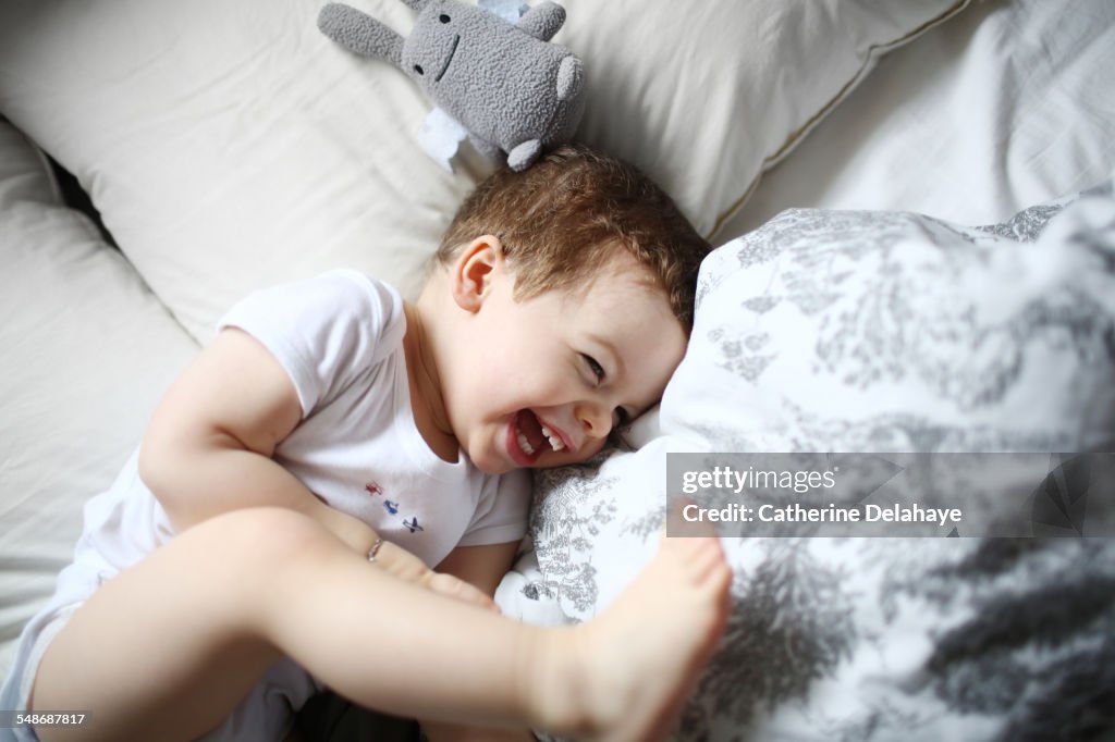A 2 years old boy laughing in a bed