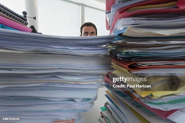 man surrounded by piles of files in office - trabajo de oficina fotografías e imágenes de stock