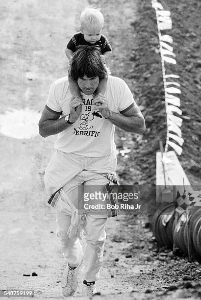 With his son Burt on his shoulders, American former professional athlete Bruce Jenner walks around the dirt race course during a break in the First...