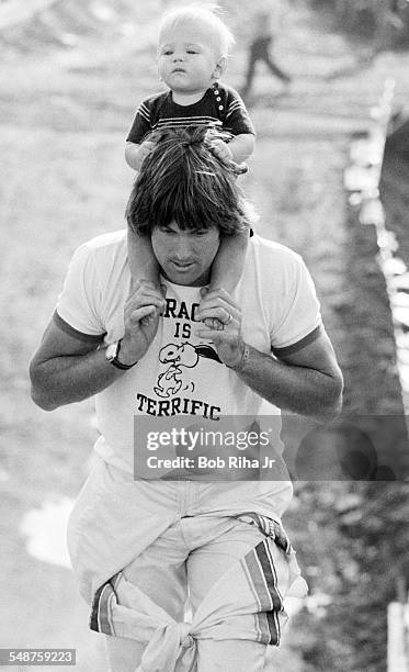 With his son Burt on his shoulders, American former professional athlete Bruce Jenner walks around the dirt race course during a break in the First...