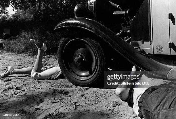 Man and woman lying with their heads under a broken car - 1938 - Photographer: Wolf Strache - Published by: 'Die Dame' 04/1938 Vintage property of...