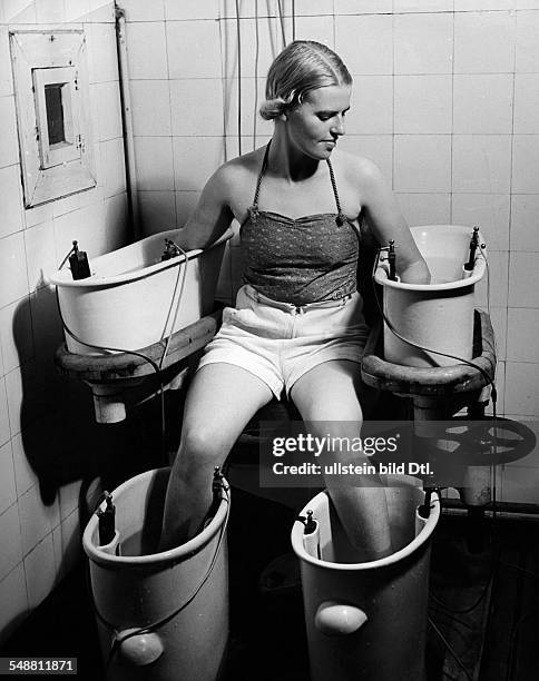 Four-cell galvanic bath: A young woman holds her arms and legs in four water bathes with electric current, this procedure has positive effect on...