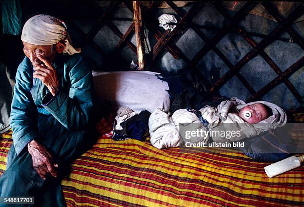 Mongolia, a grandmother watching her grandchild who is wrapped tightly in blanket. Province of Khoevsgoel.