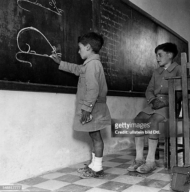 <english> View in a boys school class; 'A twelve years old boy is teaching a nine years old pupil' - ca. 1938 - Photographer: Black Star - Vintage...
