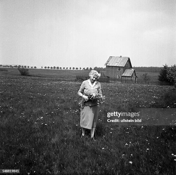 Woman on a meadow with bunch of flowers in front of a house