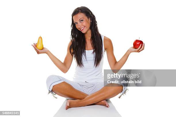 Symbolic photo healthy eating, young woman in the lotus position helding an apple and a pear in her hands