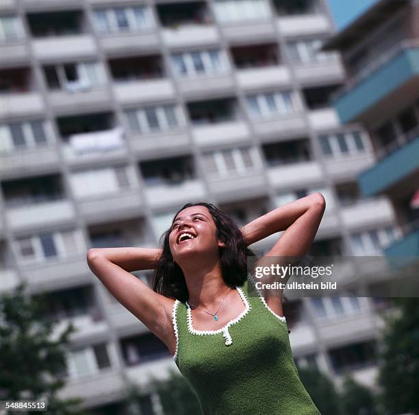 Happy young woman in front of a multi-storey apartment house - 1970s