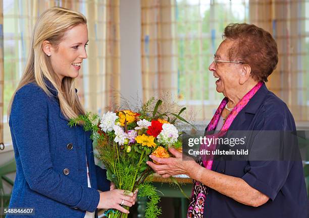 Granddaughter is visiting her grandmother an is bringing flowers -