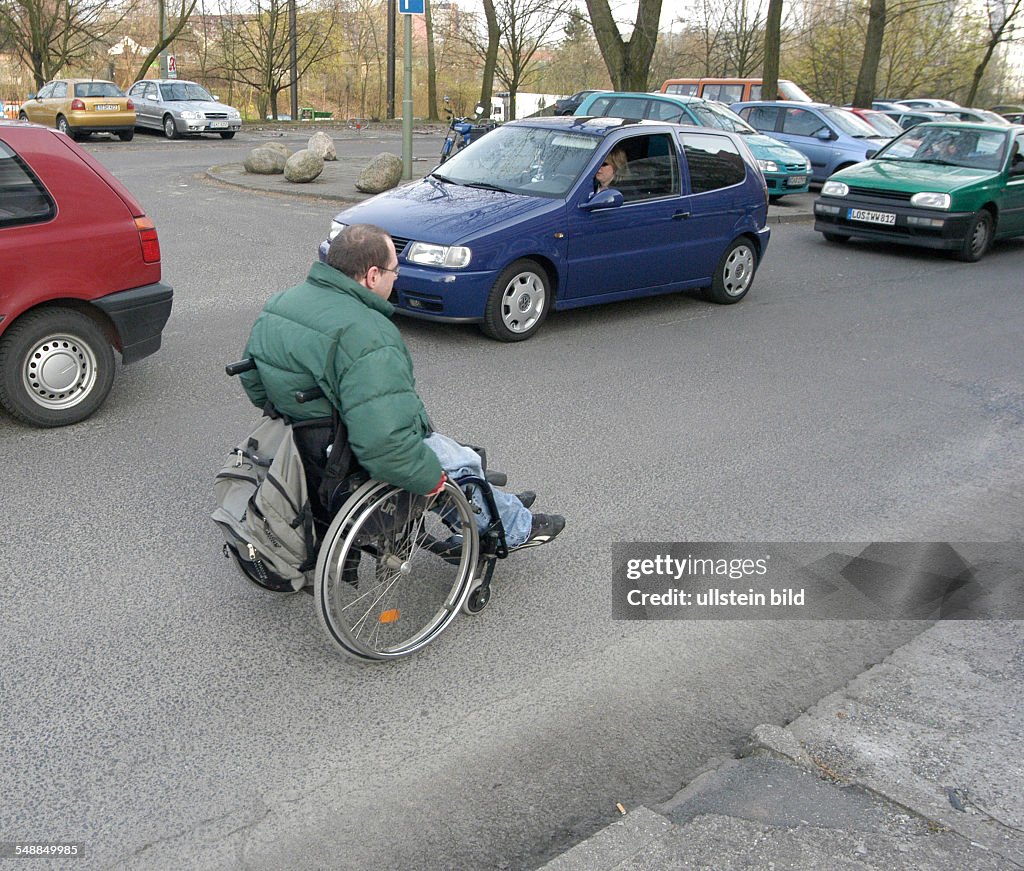 Germany Berlin - handicapped man in wheel chair is using the driving surface because of the high road kerb he cannot reach the pavement - 20.04.2006