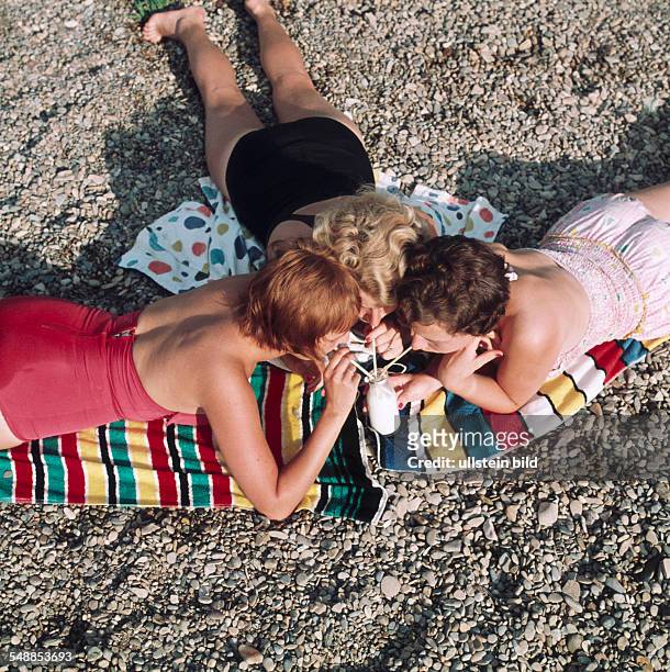 Three girls wearing bathing costume are drinking milk out of a bottle with a straw - 1950s