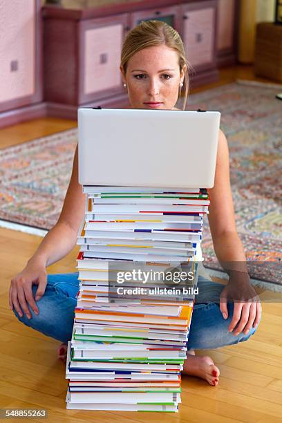 Young woman sitting behind a pack of books with a laptop on top -