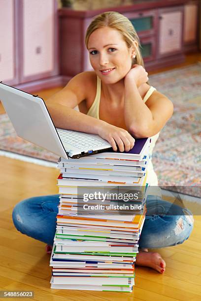 Young woman sitting behind a pack of books with a laptop on top -