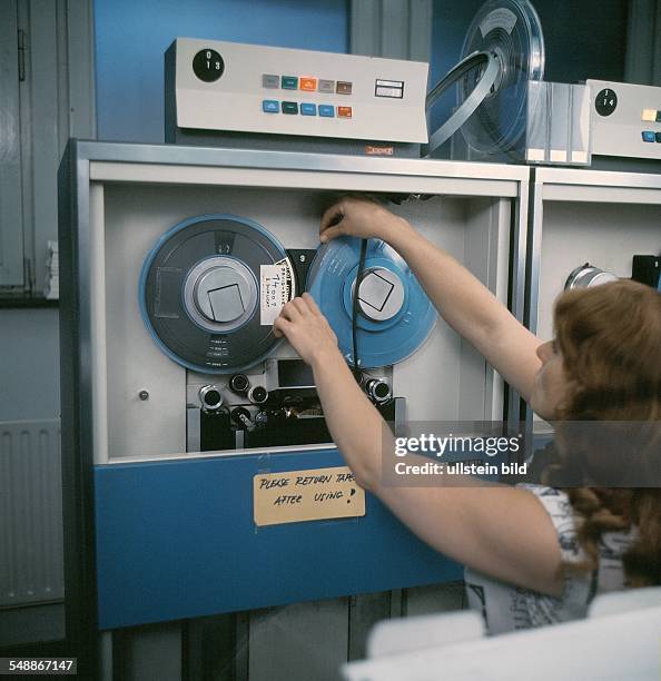 Frau legt ein Magnetband in die Magnetbandeinheit eines Computers - 60er Jahre