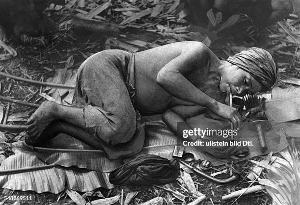 China: The New Year - celebrations: The headman of the Lahu - people recreates on big leaves, smoking an opium pipe - ca. 1942 - Photographer: Hugo...