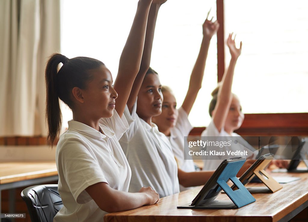 4 school girls with tablets & raised hands