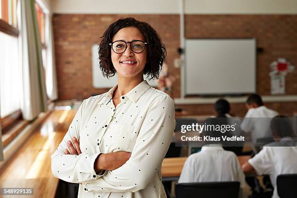 portrait of teacher in classroom, students in back - enseignante photos et images de collection