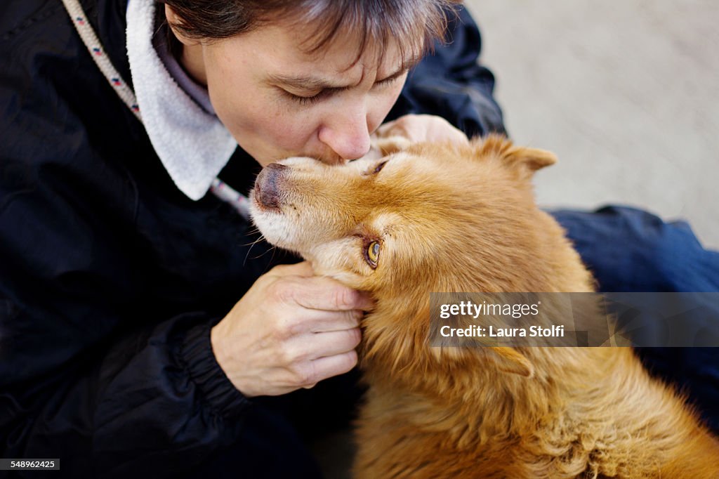 Woman kissing a little ginger dog on muzzle