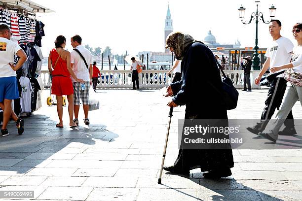 Old woman begging for money amongst tourists in Venice, Italy