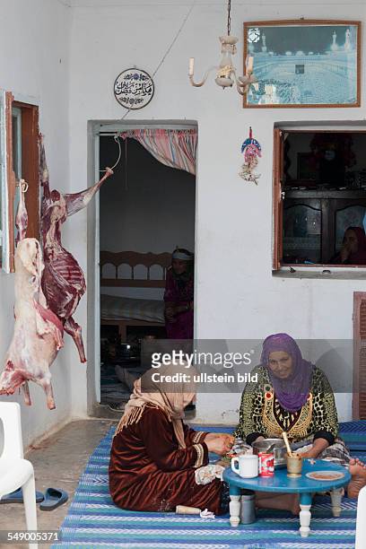 Tunisia: Women in traditional clothing preparing the meal for Eid al-Adha, slaughtered animals hang on the wall