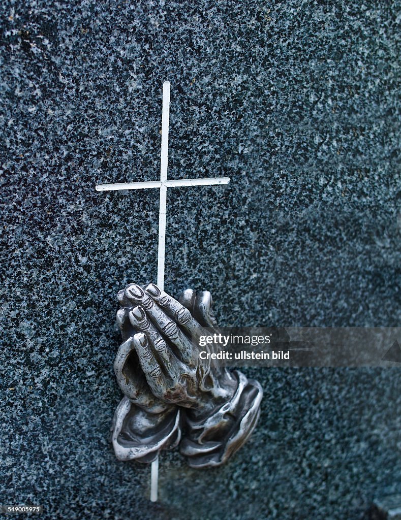 Ein Grabstein auf einem Friedhof. Betende Hände mit Kreuz