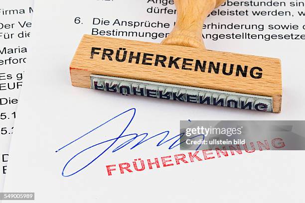 Ein Stempel aus Holz liegt auf einem Dokument. Aufschrift Früherkennung