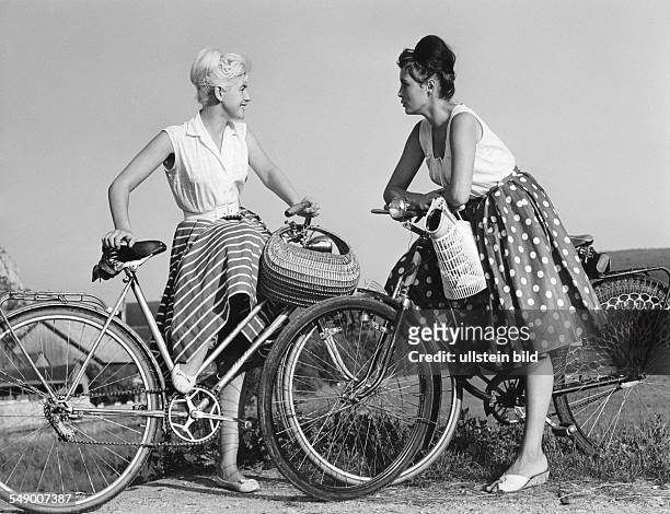 Two young women with bicycles in a talk lete fifties