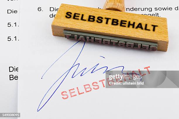 Ein Stempel aus Holz liegt auf einem Dokument. Deutsche Aufschrift: Selbstbehalt