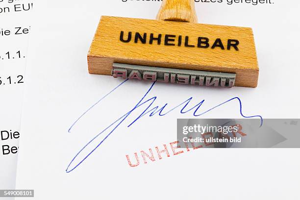 Ein Stempel aus Holz liegt auf einem Dokument. Deutsche Aufschrift: Unheilbar