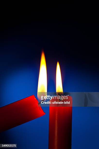 Eine rote Kerze wird mit einem Streichholz angezündet.