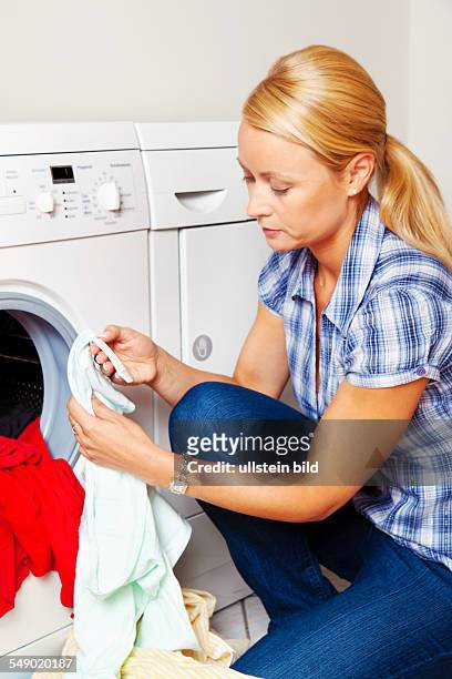 Hausfrau mit Wäsche an der Waschmaschine liest die Wascheinleitung auf dem Etikett eines Kleidungsstücks