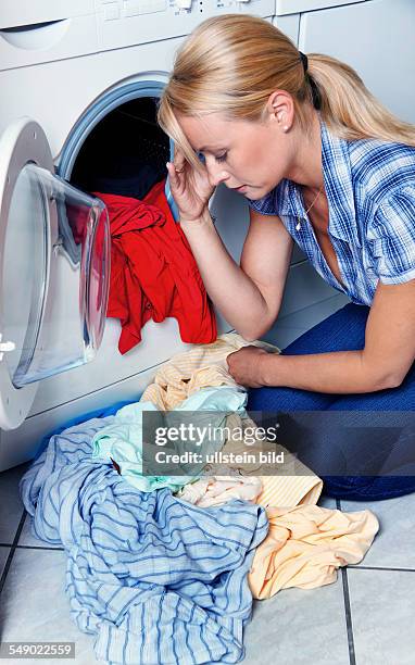 Eine junge Frau mit Wäsche an der Waschmaschine ist erschöpft
