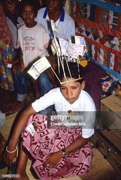 Philippines, Sulu sea: A circumcised fourteen-year-old Badjao boy with a headdress made of banknotes on stick to look like flags on the island Bongao.