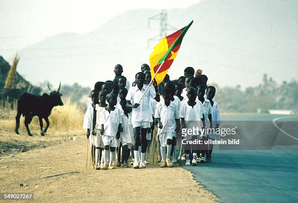 Cameroon: A class of students carrying the national flag march down a road built by the Germans. -