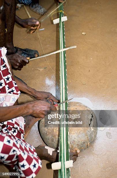 Benin, Mono Region, Houeyogbe: Men playing a Didin Nagbo, an instrument made from a palm branch, two corn cobs and a calabash placed on ashes, it is...