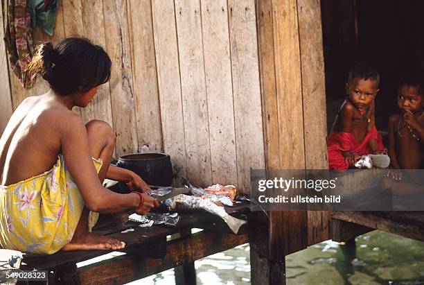 Philippines, Sulu sea: A Badjao woman preparing fish on a platform in front of her stilted house on the island of Bongao.