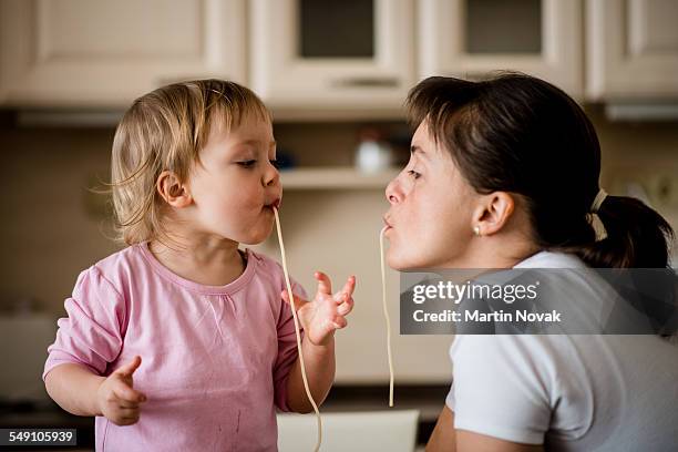mother and child eating spaghetti together - spaghetti foto e immagini stock