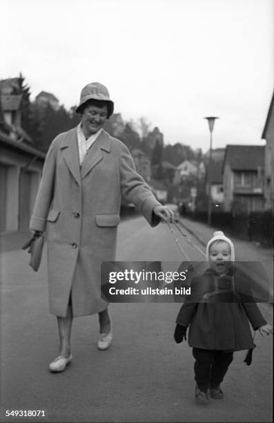 Germany, about 1960: A mother takes a walk with her child. She holds it with a leading reins for children.