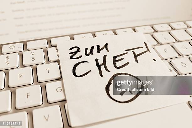 Ein Notizzettel liegt auf der Tastatur eines Computers zur Erinnerung: Zum Chef