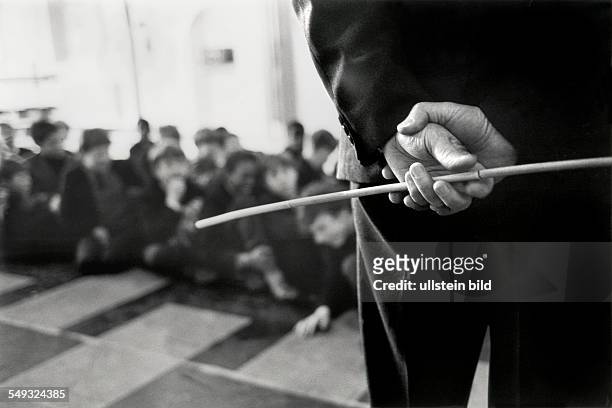 Great Britain, England, London, Battersea Secondary School, pupils sitting on the floor of the assembly hall, teacher with cane