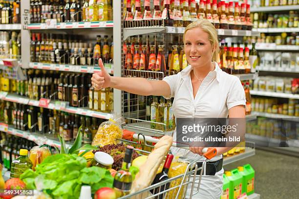 Eine junge Frau beim Einkauf mit einem Einkaufswagen in einem Supermarkt.