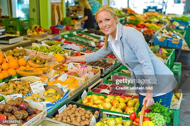 Eine junge Frau kauft Obst und Gemüse auf einem Wochenmarkt. Frische und gesunde Ernährung.