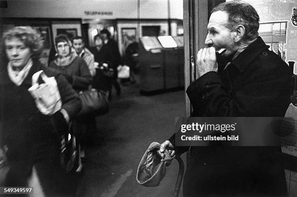 Great Britain, England, London, beggar playing mouth-organ at entrance of Underground tube-station.