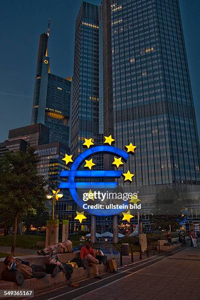 Illuminated Euro symbol and homeless people in front of the Eurotower, European Central Bank in Frankfurt am Main by night.