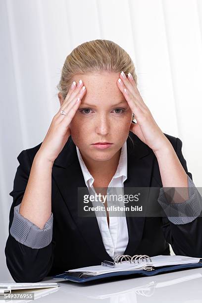 Eine junge Frau mit Migräne und Kopfschmerzen sitzt in einem Büro.