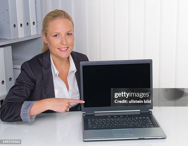 Eine junge erfolgreiche Frau im Büro deutet auf einen Laptop. Textfreiraum am Bildschirm