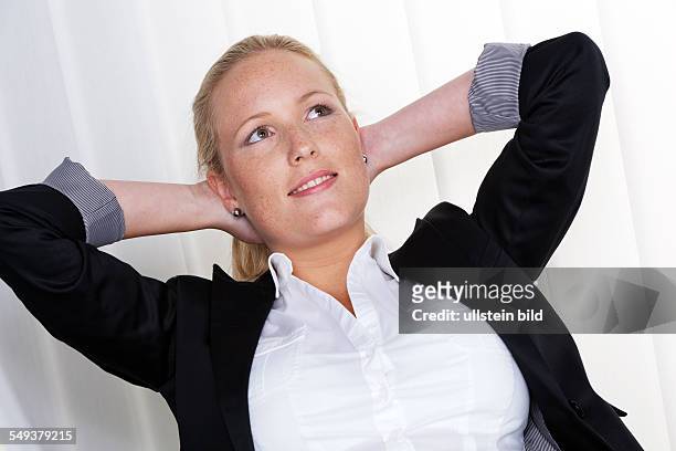 Eine nachdenkliche Geschäftsfrau sitzt auf ihrem Sessel und hat die Hände im Nacken verschränkt