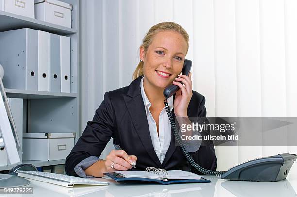Eine freundliche Frau telefoniert an ihrem Schreibtisch im Büro und notiert Termine im Kalender